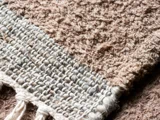 Nærbillede af et struktureret, vævet brunt stoftæppe med synlige fibre og en flettet kant, der viser detaljeret vævning og løse tråde.