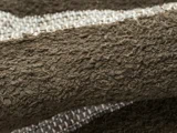 Nærbillede af et struktureret, brunt vævet stof med synlige fibre og en hvid stribe, der løber gennem mønsteret.