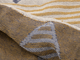 Nærbillede af vævet stof med brune, hvide og blå tråde med geometriske mønstre og striber. Stoffet virker struktureret og let krøllet.