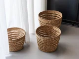 Tre flettede kurve i forskellige størrelser er anbragt på et gråt gulv i nærheden af hvide gardiner og en sort væg.