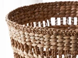 Nærbillede af den øverste kant af en flettet kurv, der viser dens strukturerede, sammenflettede naturlige fibre med lys, der skinner gennem hullerne.