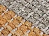 Nærbillede af en vævet måtte med sammenflettede grå og brune fibre, der viser materialets detaljerede struktur og mønster.