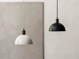 To kuppelformede pendler, en hvid og en sort, hænger fra loftet mod en minimalistisk, lys vægbaggrund.