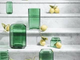 Grønne glasvaser og -krukker er opstillet på hvide marmortrapper, og der ligger flere hele citroner og citrongrene spredt imellem dem.