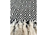 Sort og hvidt tekstil med et geometrisk diamantmønster med lyse frynser langs kanten.