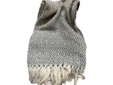Et foldet, vævet tæppe med et gentagende diamantmønster i grå og hvid, afsluttet med frynsede kanter.