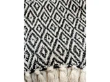 Nærbillede af et vævet tekstil med et sort og hvidt diamantmønster og kvaster langs den nederste kant.