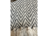 Nærbillede af et vævet stof med et gråt og hvidt zigzag-sildbensmønster og frynsede kvaster langs den nederste kant.