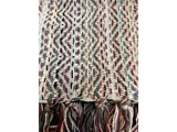Nærbillede af et vævet tekstil med zigzagmønster i cremefarvede, grå og rødbrune nuancer og med knyttede, flerfarvede frynser i den nederste kant.