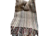 Et vævet tekstil med indviklede geometriske mønstre i jordfarver og flerfarvede frynser langs den nederste kant.
