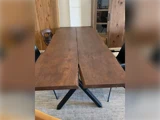 Et spisebord i træ med en naturlig flænge i midten, sorte metalben og sorte stole omkring det, placeret på et beige tæppe.