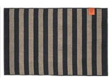 Rektangulær bademåtte med skiftevis sorte og beige lodrette striber og et orange mærke med logo i øverste højre hjørne.