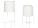 To moderne hvide cylindriske plantekasser på stativer i forskellige højder, begge med fire lige ben og tværstænger til støtte.