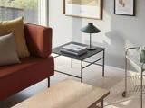 En moderne stue med en rustfarvet sofa, neutrale puder, et sort sofabord med bøger og en lampe, kunstværker på væggen og en lille rullevogn ved siden af.