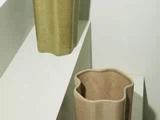 To skulpturelle keramikvaser med bølgede kanter - en olivengrøn og en beige - står på forskudte hvide hylder mod en neutral baggrund.