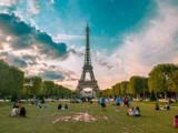 Folk slapper af og går tur i en græsklædt park nær Eiffeltårnet i Paris med en levende himmel og træer i baggrunden.