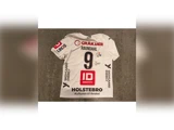 Hvid håndboldtrøje til spilleren Raundahl, nummer 9, med forskellige sponsorlogoer og en signatur på ryggen.