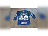 En blå ishockeystrøje med navnet DILLING LINDE og nummeret 88 på ryggen samt flere sponsorlogoer. Strøjen ligger fladt på et betongulv.