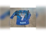En blå og sort sportstrøje med navnet AMOROSA, nummer 7 og flere sponsorlogoer, herunder SPECIAL BUTIKKEN, på ryggen.