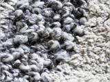 Et nærbillede af et tæppe med høj luv, hvor der er partier med tykt, løkkeformet gråt og sort garn ved siden af områder med strukturerede cremefarvede fibre.