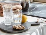 To klare glas stablet oven på hinanden, det ene glas med vand, en citron og ingefærrod på et rundt stenbræt.