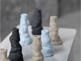 Små, abstrakte keramiske vaser i afdæmpede sorte, blå og beige farver, anbragt på en hvid overflade med en sløret grå baggrund.