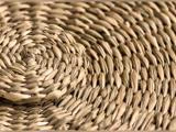 Nærbillede af flettet strå, der viser den detaljerede struktur og det mønster, der består af overlappende naturfibre, der er anbragt i cirkulære former.