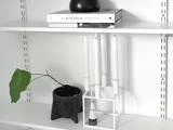 En minimalistisk hvid hylde med bøger, en sort vase, en potteplante med et enkelt blad og en moderne hvid lysestage.