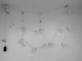 En hvid lyskæde med blottede pærer er draperet i et løst zigzagmønster og fastgjort til en hvid væg. Et sort stik er synligt til venstre.