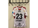 En hvid og rød sportstrøje med nummer 23 og navnet Lützhøft hænger på en vægkrog og er prydet med forskellige sponsorlogoer.