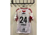 En hvid og rød sportstrøje med nummer 24 og navnet Edwige hænger på en sort vægkrog. På ryggen ses forskellige sponsorlogoer.
