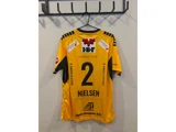 En gul sportstrøje med nummer 2 og navnet »Nielsen« på ryggen, der hænger på en krog. Trøjen er prydet med forskellige sponsorlogoer.