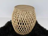 Et rundt, flettet rattan-sidebord med gitterdesign står på et sort, loddent tæppe mod en almindelig hvid baggrund.
