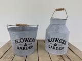 To metalbeholdere med træhåndtag mærket FLOWERS & GARDEN står på en træplade; den ene er en spand, og den anden er en dunk.