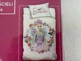 Et sengesæt med Barbie-tema med en eventyrlig Barbie med vinger, omgivet af blomster og sommerfugle, på en lyserød baggrund med ordet Barbie skrevet på dynen og puden.