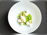 En hvid tallerken med en moderne dessert: grøn sauce, klatter af fløde, små marengs, mynteblade og en oval kugle is, kunstnerisk arrangeret.