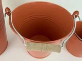 En orange metalspand med træhank, set ovenfra, med dele af to lignende spande synlige på hver side.