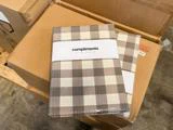 To pakker med beige og hvidt ternet sengetøj, indpakket i plast, mærket Compliments seersucker-sengetøj.