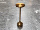 Et lille, rundt sidebord i metallisk guld står på et gråt betongulv.