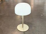 En moderne, hvid bordlampe med en ribbet, kuppelformet lampeskærm står på en rund, beige fod oven på en glat, grå overflade.