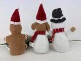 Tre plysfigurer - en peberkagemand, en hund og en snemand - sidder med front mod hinanden iført festlige hatte og tørklæder på en almindelig hvid baggrund.