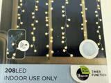 Lyskæder med runde pærer hænger foran et vindue. På emballagen står der 208 LED, kun til indendørs brug og mulighed for timerfunktion.