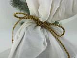 Et gennemsigtigt hvidt stof bundet med en guldsnor, dekoreret med grønne fyrretræsgrene i baggrunden.