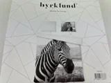 Et sengesæt med sort og hvidt zebraprint vises på emballagen, der er mærket byrklund basics for living med geometriske linjer i baggrunden.