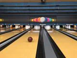 En rød bowlingkugle ruller ned ad en bane mod hvide kegler på en bowlingbane med farverig kuglegrafik på bagvæggen.