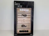 En rektangulær æske med spillet The Shuffle Battle, der viser en træplade med pucker og spilmarkeringer på forsiden. Egnet til børn fra 8 år og opefter.