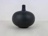 En lille, rund, mørkegrå keramikvase med smal hals, placeret på en lys overflade mod en almindelig hvid baggrund.