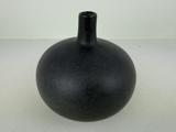 En rund, matsort keramikvase med smal hals og lille åbning, placeret på en lys overflade mod en ensfarvet baggrund.