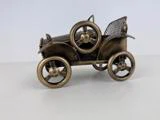 En lille, metallisk model af en gammeldags bil med store hjul, et reservehjul på siden og et netlignende bagsæde.