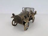 En lille metalmodelbil i vintage-stil med netgitter og egerhjul på en almindelig hvid overflade.